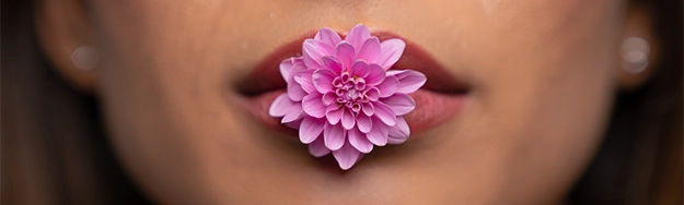 gros plan sur une bouche féminine tenant une fleur violette entre ses lèvres