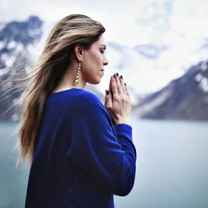 une femme main jointe pour une prière devant un lac et des montagnes eneigées